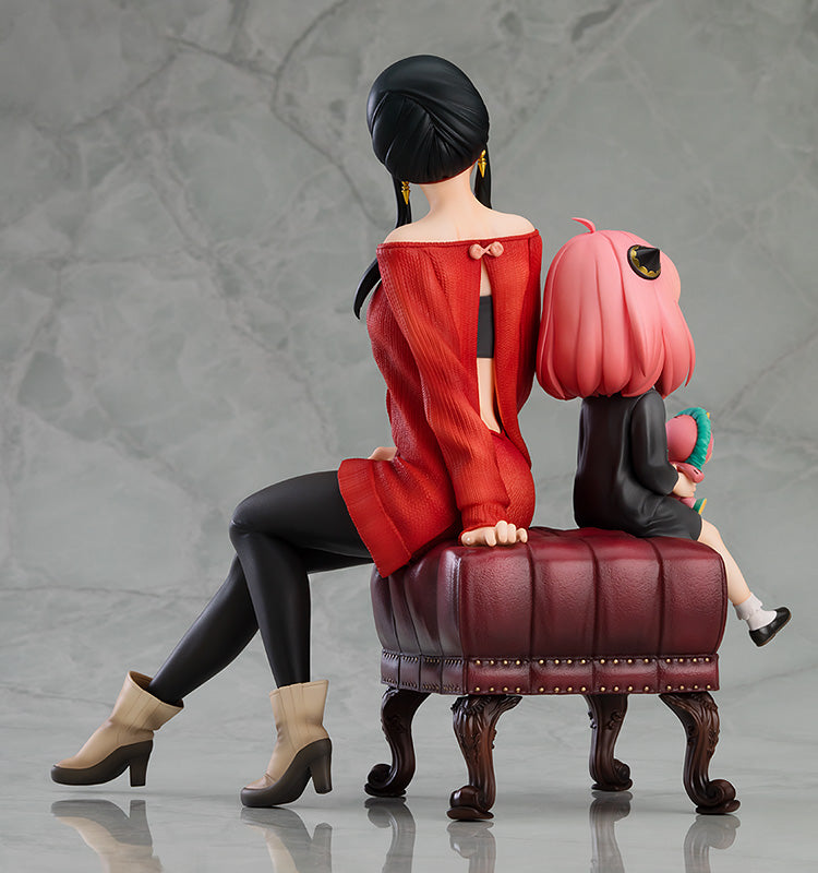 Side profile view of Good Smile Company SPY x FAMILY Anya & Yor 1/7 scale figure, Yor in backless red dress with Anya beside her on velvet ottoman, detailed legs and boots
